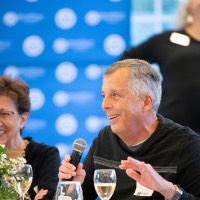 Man smiling as he talks into microphone, woman next to him smiles also